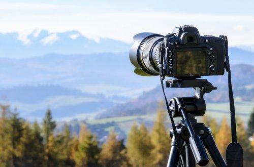 MIRRORLESS CAMERA MOUNTED ON TRIPOD WITH MOUNTAINS FIELDS AND FOREST